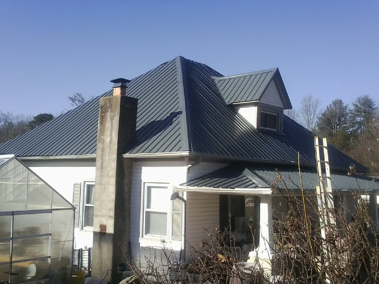 Dark blue standing seam metal roof on a white farmhouse with dormer — Slate & Tile Roof Repair by Roofing Brothers in Cuthbert