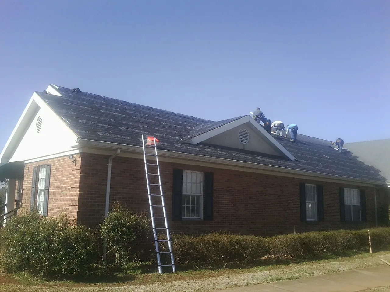 Crew tearing shingles off a brick ranch roof with a ladder set — Emergency Roof Repair work by our crew in Cuthbert