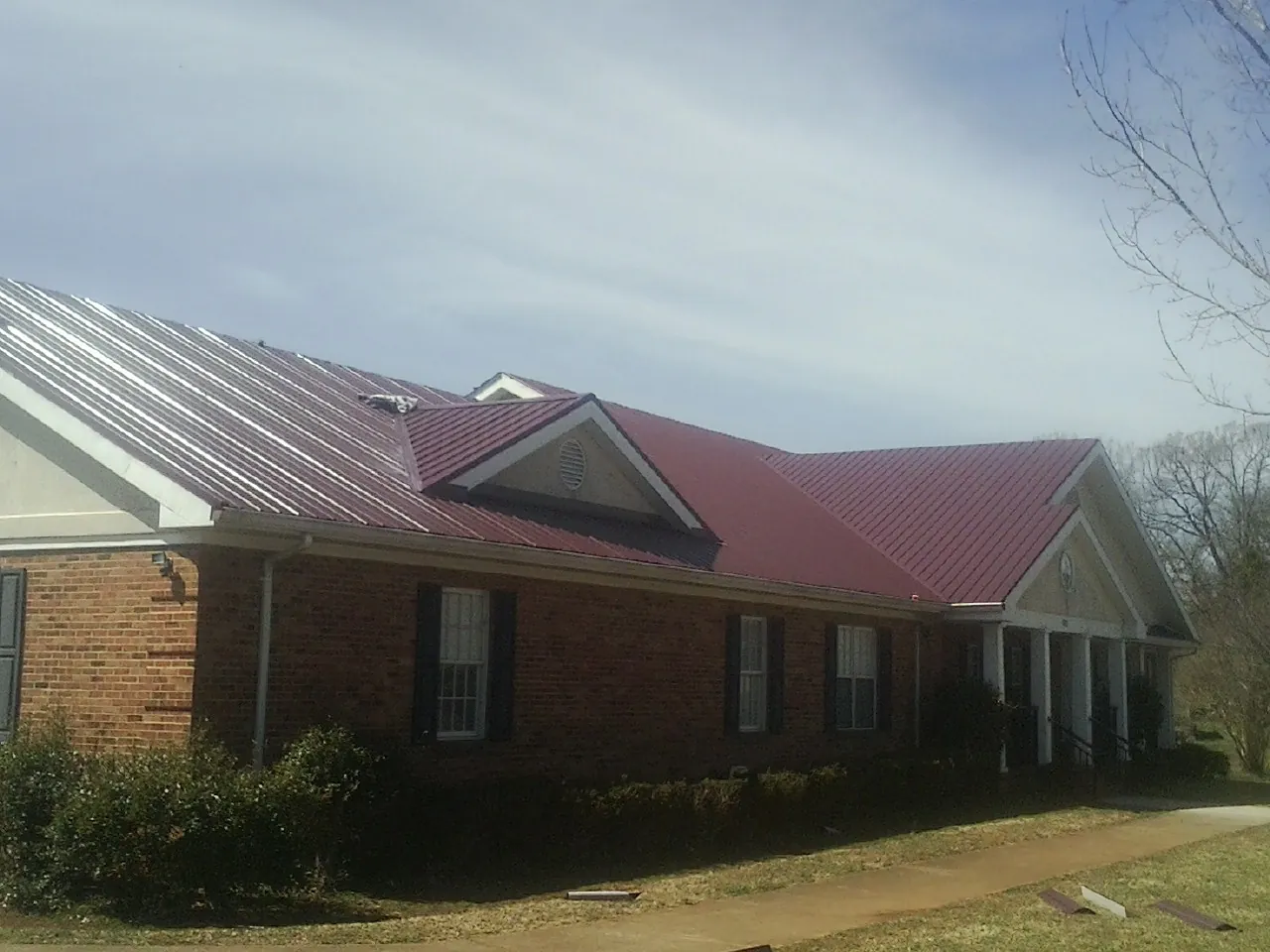 Red metal roof with gabled entries on a long brick building, from a Hail Damage Roof Repair job in Cuthbert