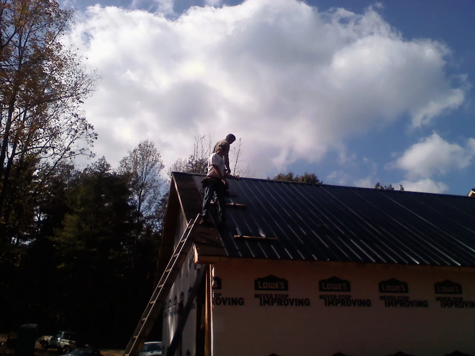 Roofer fastening dark metal panels high against a cloudy sky, from a Roof Inspection job in Cuthbert