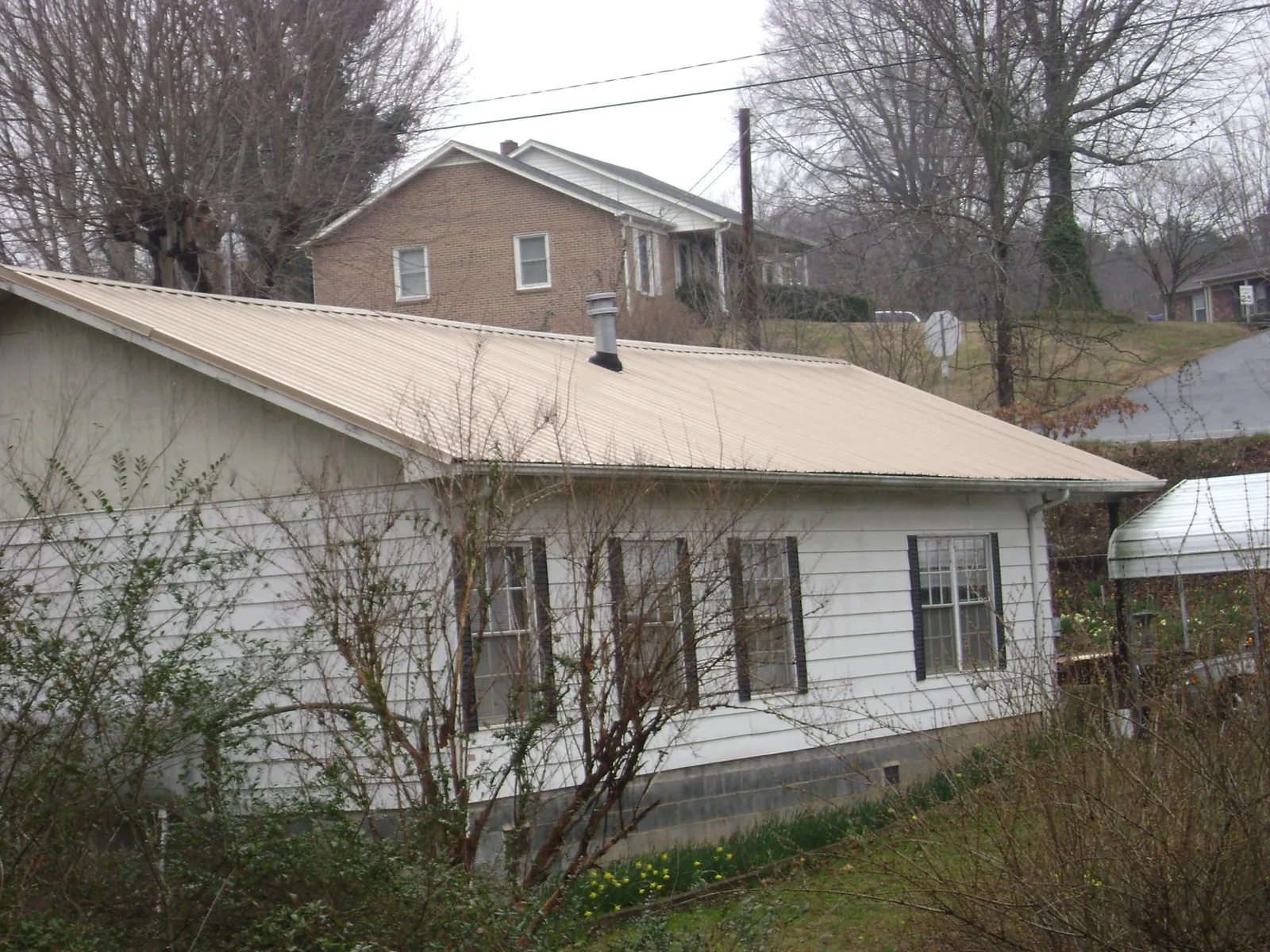 Tan metal roof on a white sided house set into a hillside — Commercial Roofing by Roofing Brothers in Cuthbert